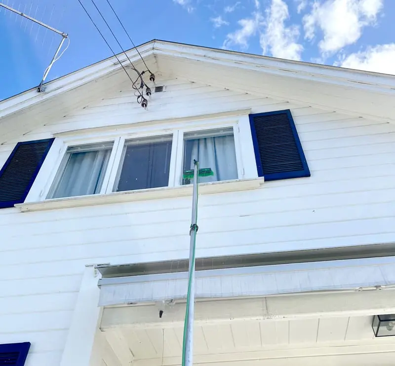 Vindusvask med teleskopstang på et hvitt trehus